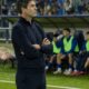 Allenatore a bordocampo con il suo assistente durante una partita serale, con i giocatori in panchina alle loro spalle