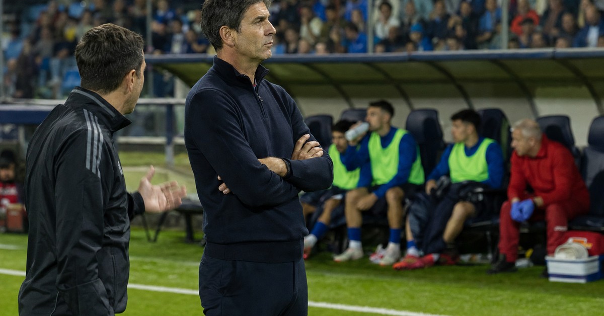 Allenatore a bordocampo con il suo assistente durante una partita serale, con i giocatori in panchina alle loro spalle